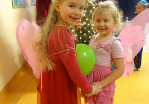 Dwie dziewczynki tańczą z balonem ułożonym pomiędzy brzuchami.